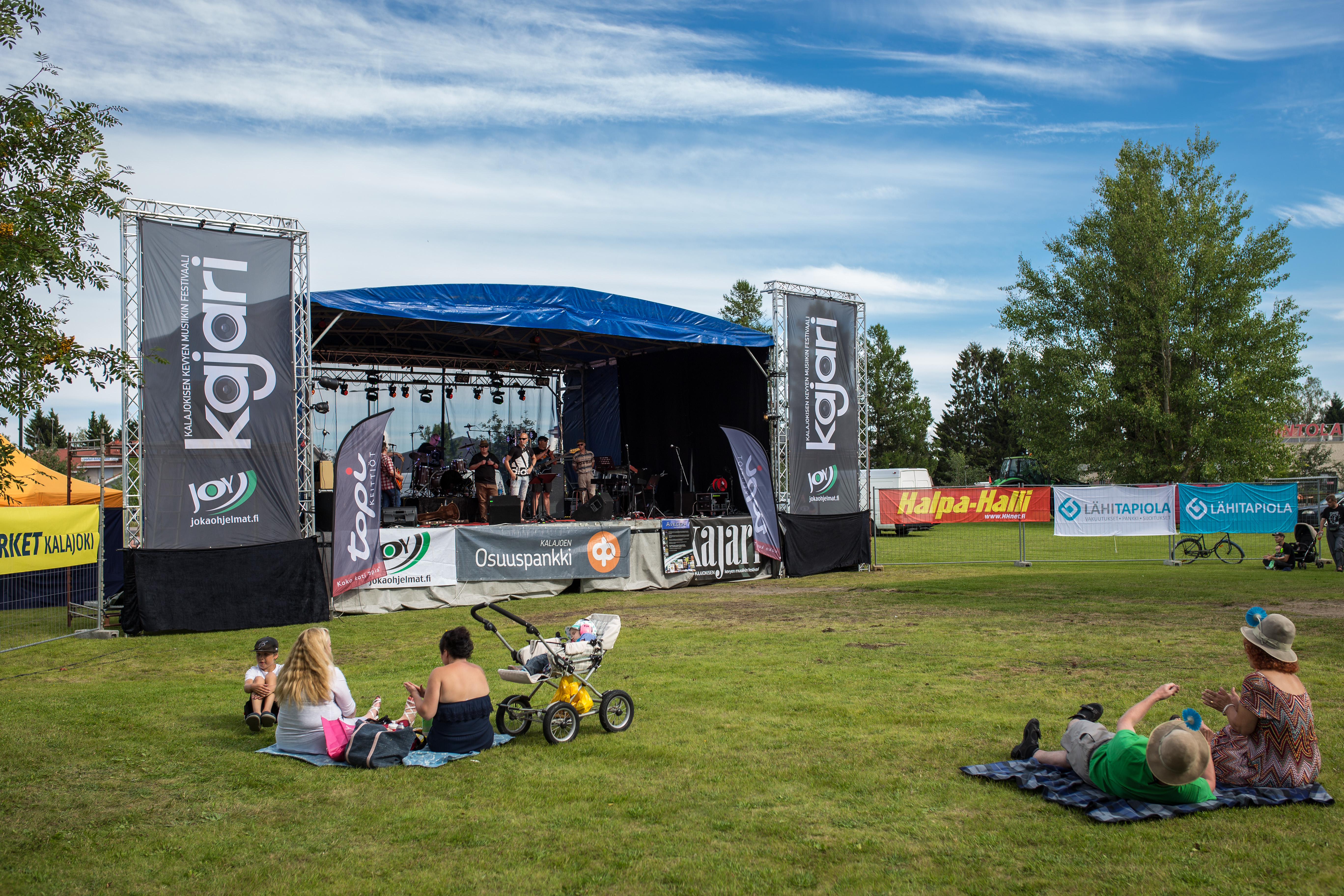 Ihmisiä istuu ruohikolla musiikkikonsertissa puistossa