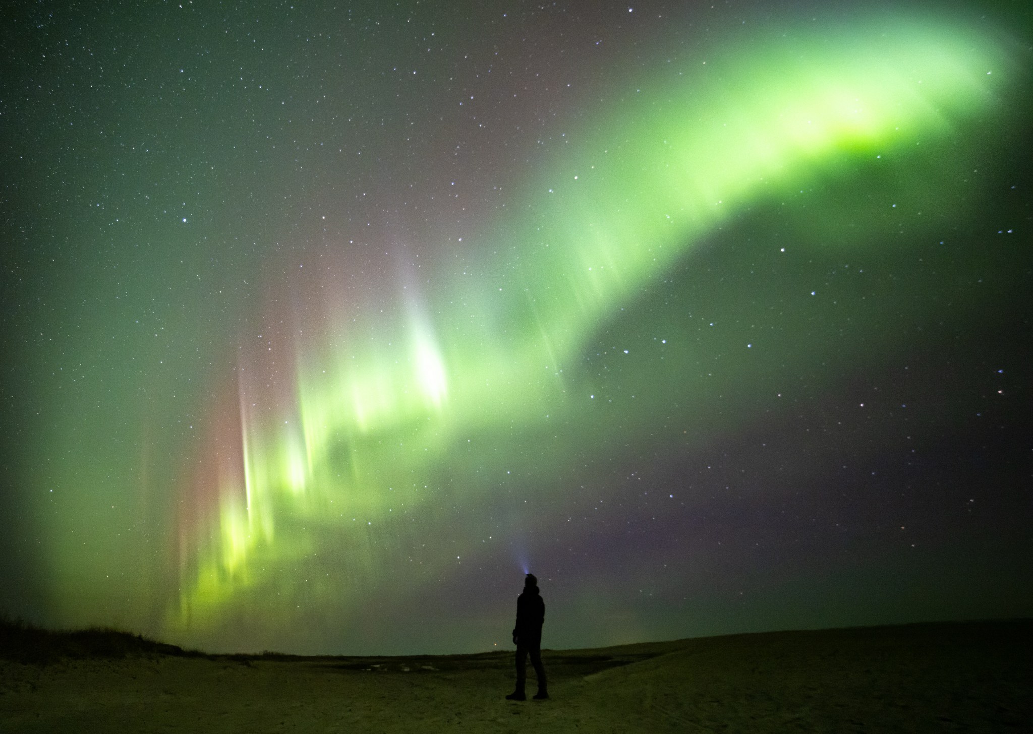 Ihminen meren jäällä otsalampun kanssa katselemassa revontulia