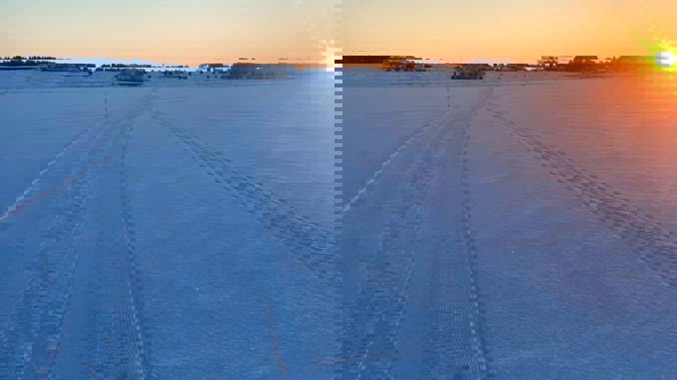 Kuvassa aurinko laskee lumiseen latumaisemaan