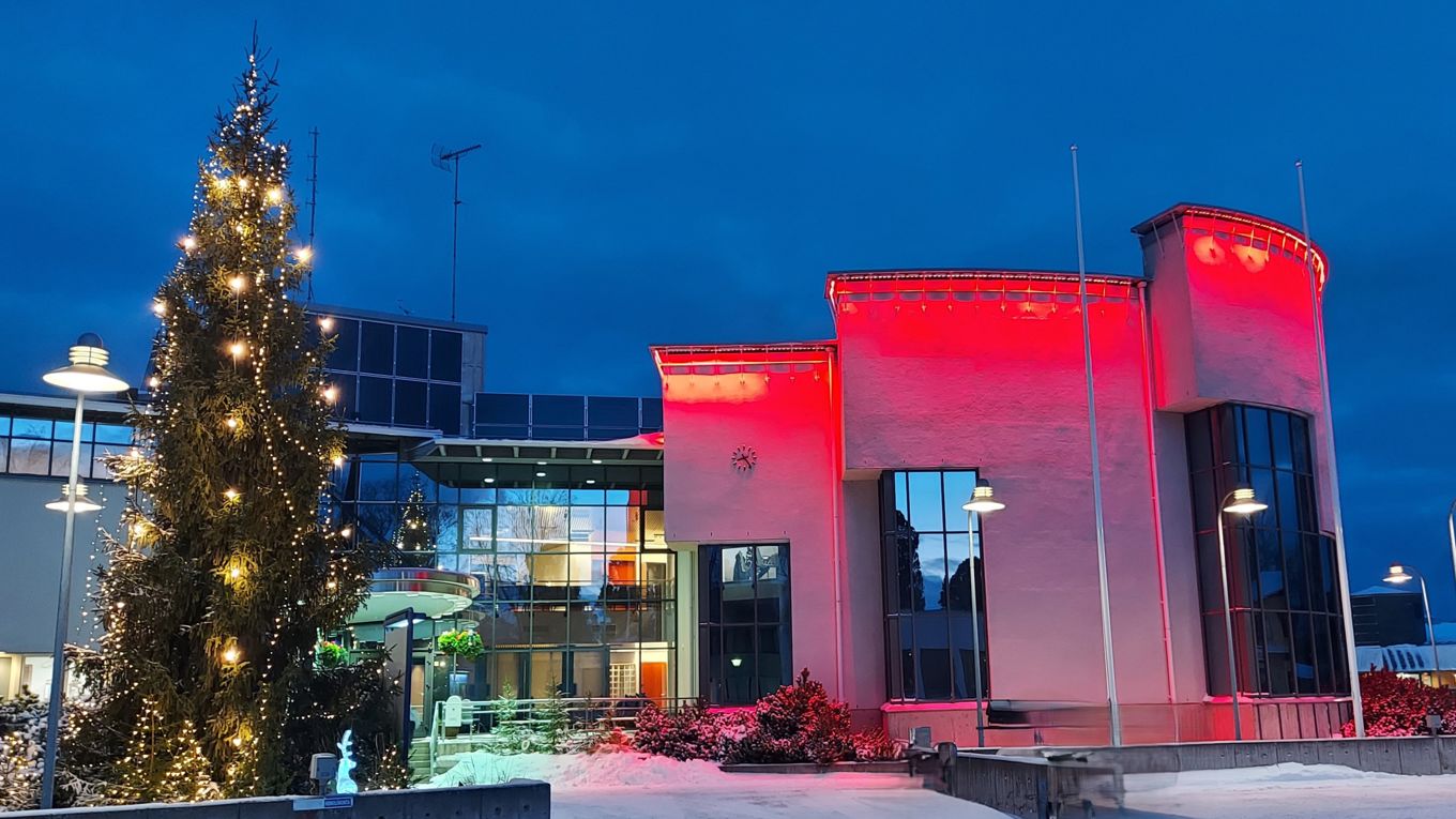 kaupungintalo punaisissa valoissa ja pihalla joulukuusi