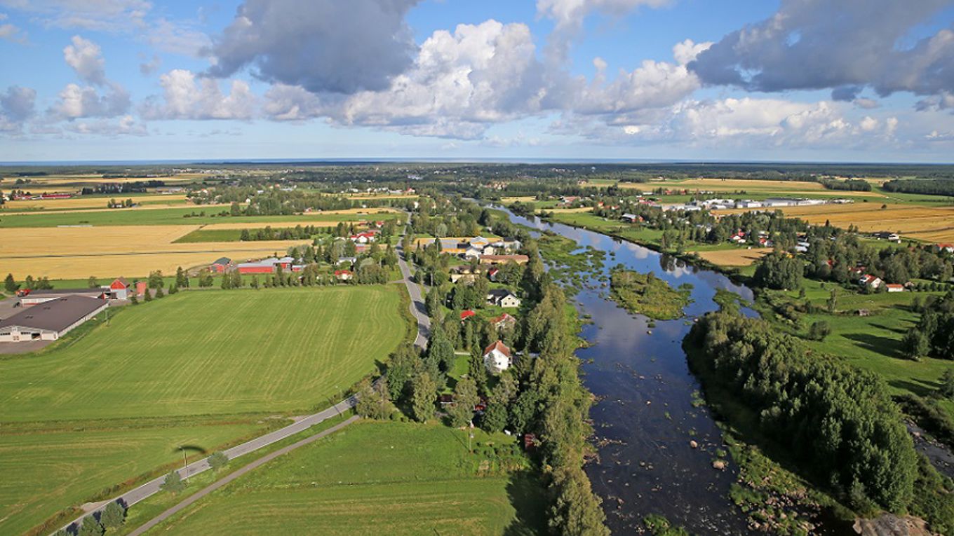 Kuva: jokimaisema, peltoa, taloja, taivas, poutapilvejä