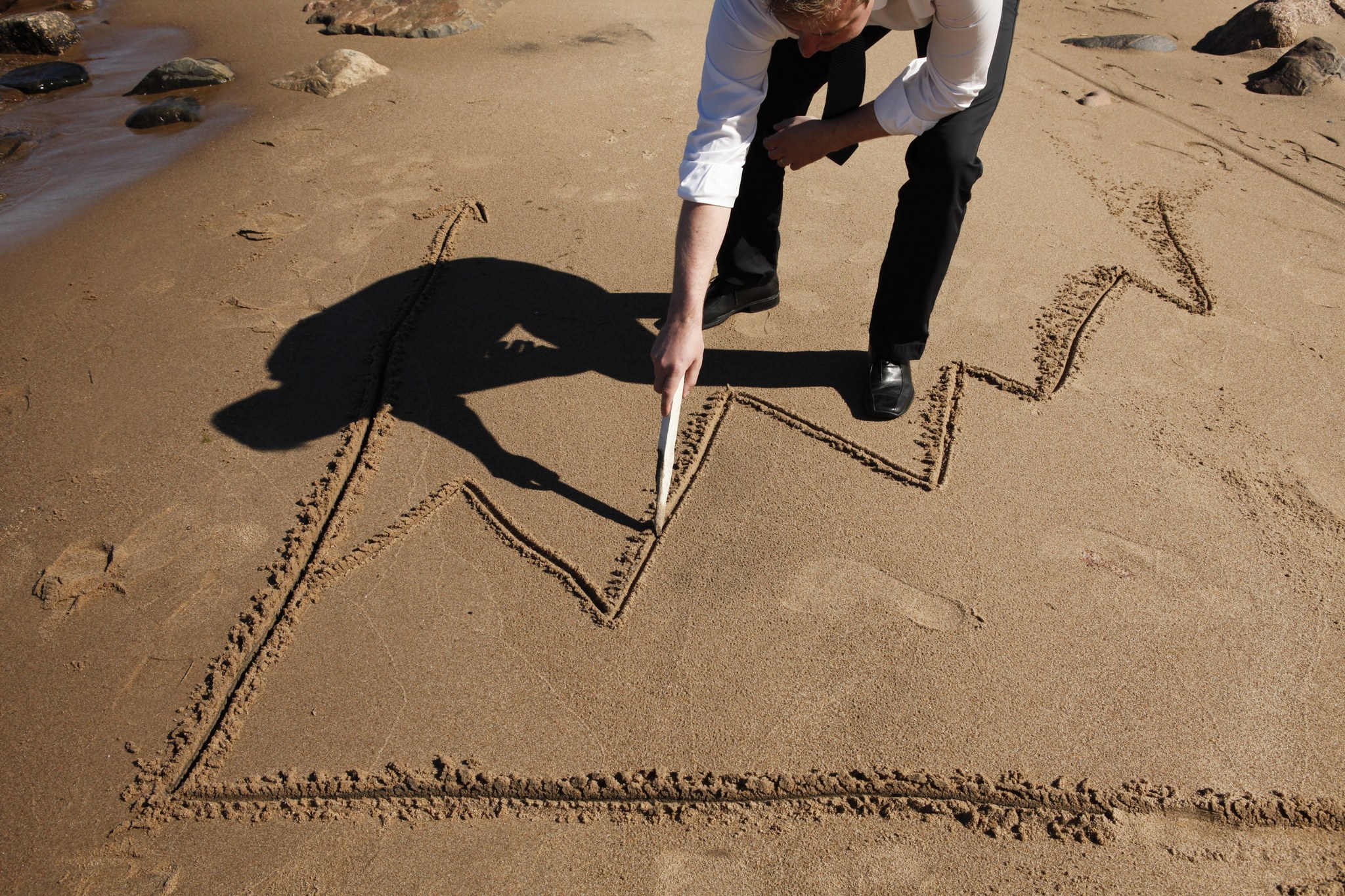 Henkilö piirtää kaaviota hiekalle.