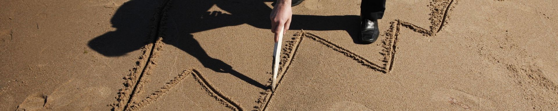Henkilö piirtää kaaviota hiekalle.