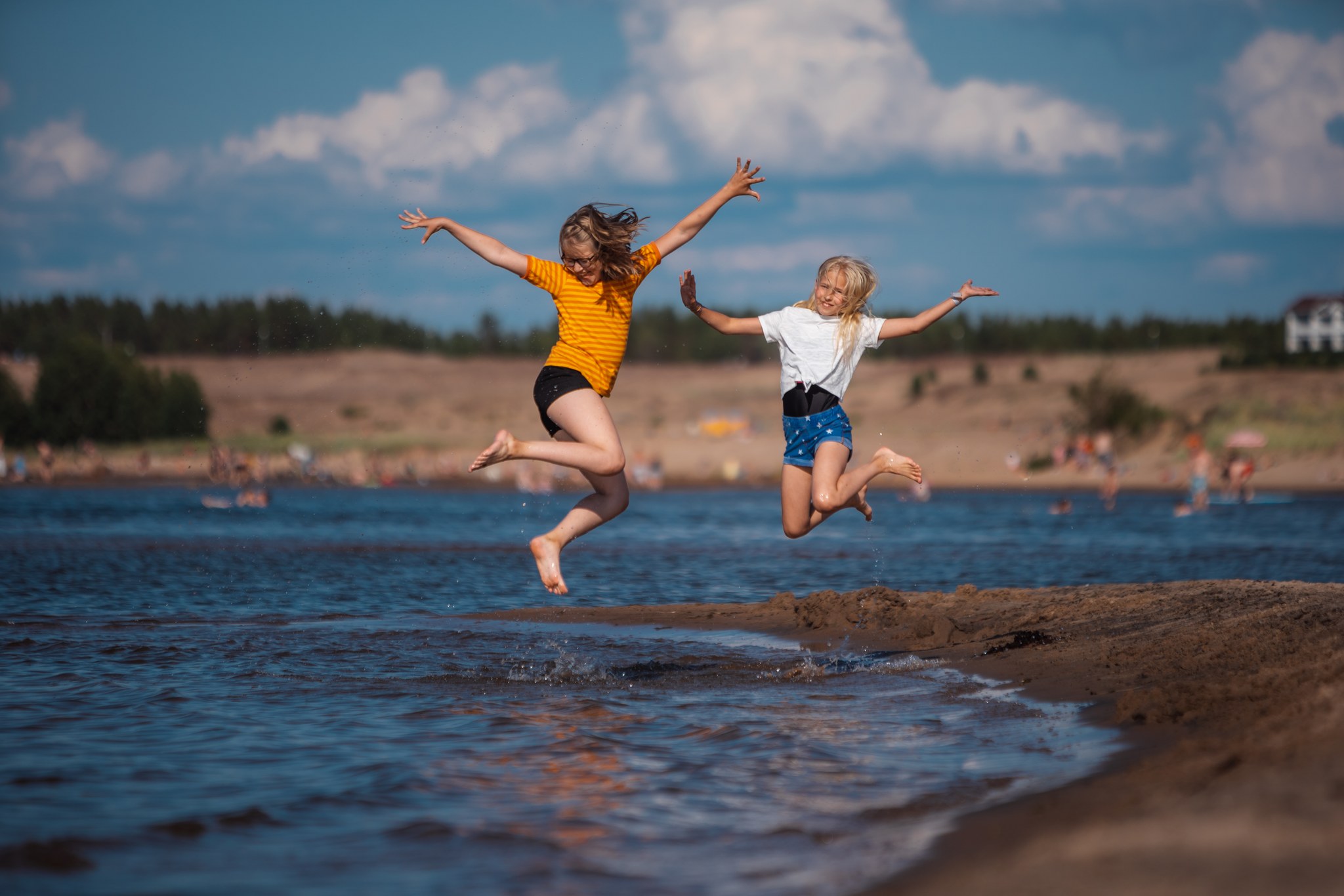 Kaksi tyttöä hyppäävät ilmaan merenrannassa. 
