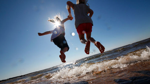 Kaksi lasta hyppii vedessä auringon paistaessa.