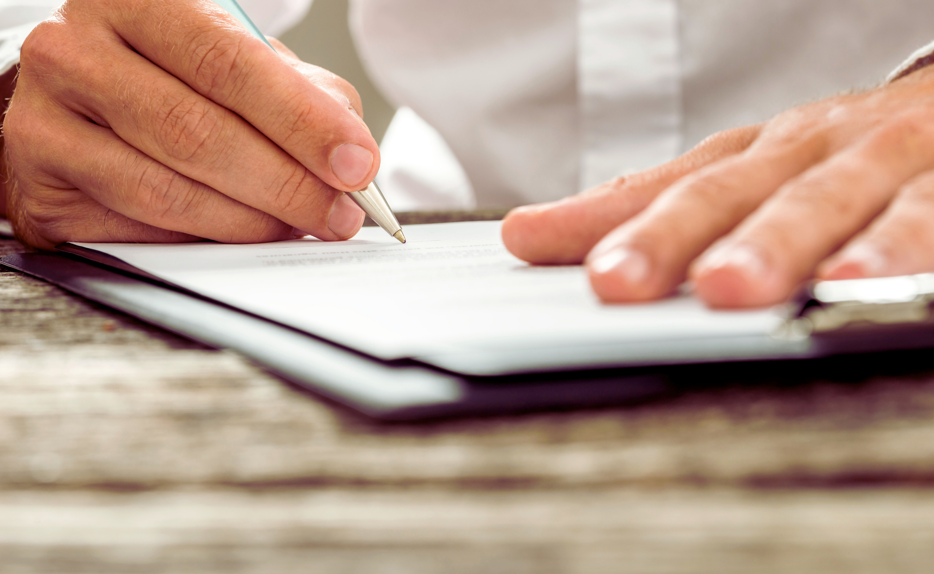Paperipino pöydällä, jota kädet pitelevät ja kirjoittavat kynällä tekstiä.