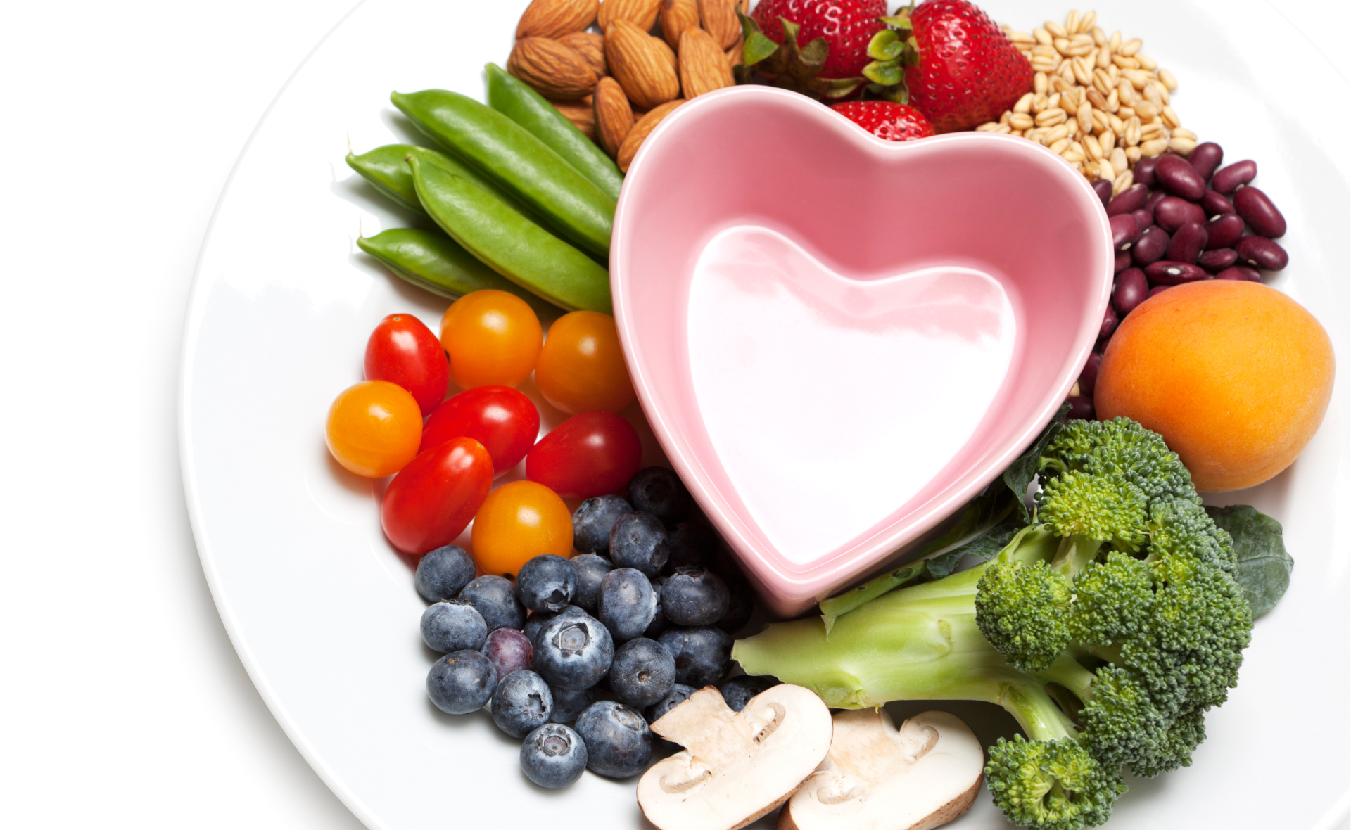 Kasviksia, marjoja ja siemeniä sydämenmuotoisen lautasen ympärillä.